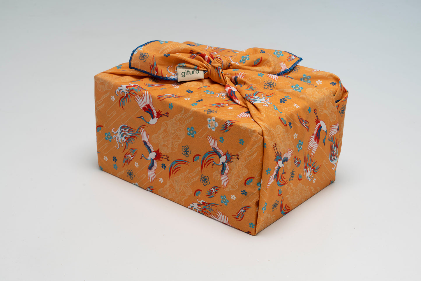 Geschenk verpackt mit dem Geschenktuch Kuren – orange mit Kranichmotiv im Furoshiki-Stil
