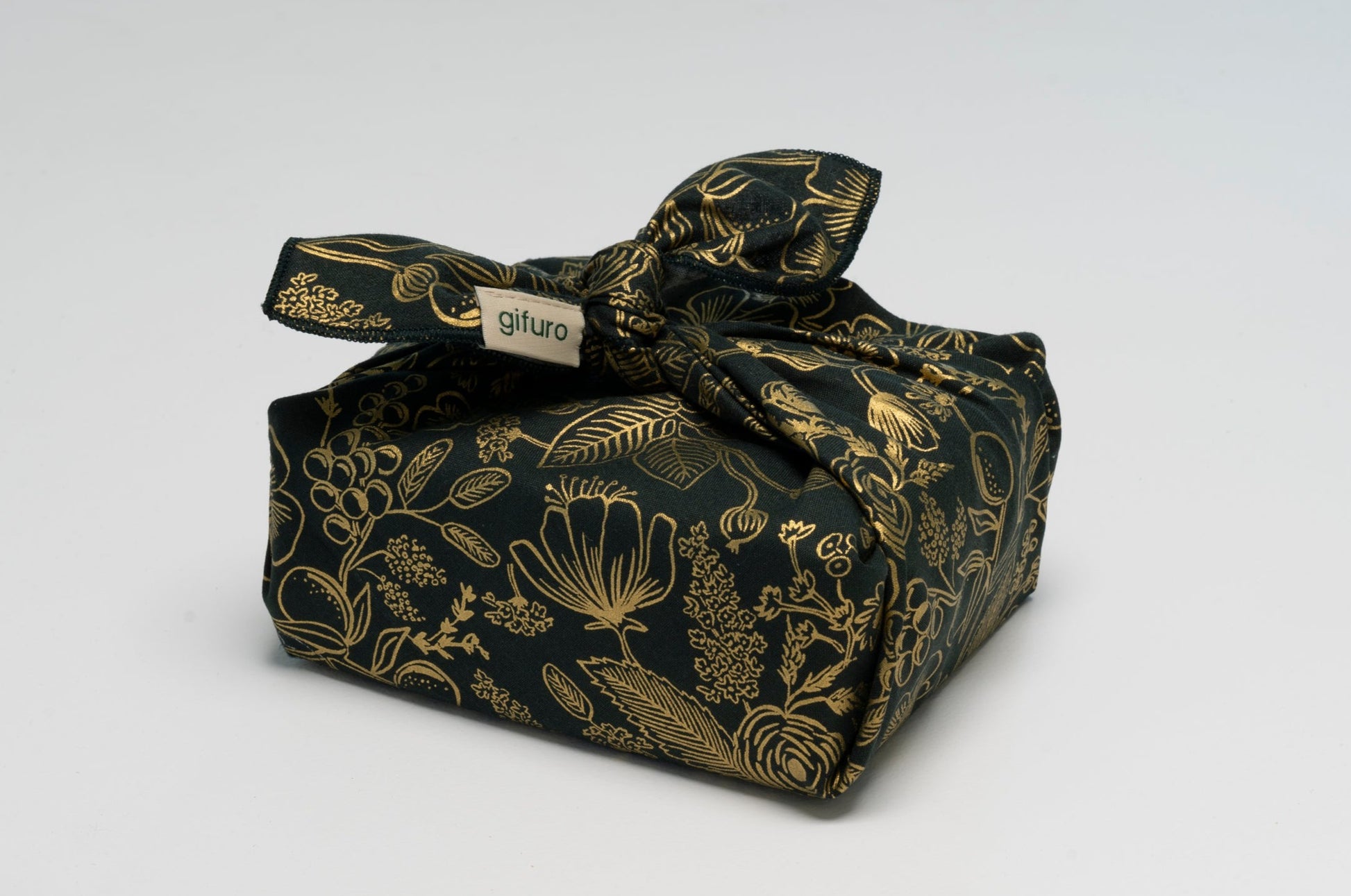 Geschenk verpackt mit dem Geschenktuch Holly – dunkelgrün mit goldenen Blumen im Furoshiki-Stil