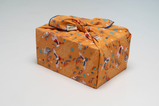 Geschenk verpackt mit dem Geschenktuch Kuren – orange mit Kranichmotiv im Furoshiki-Stil